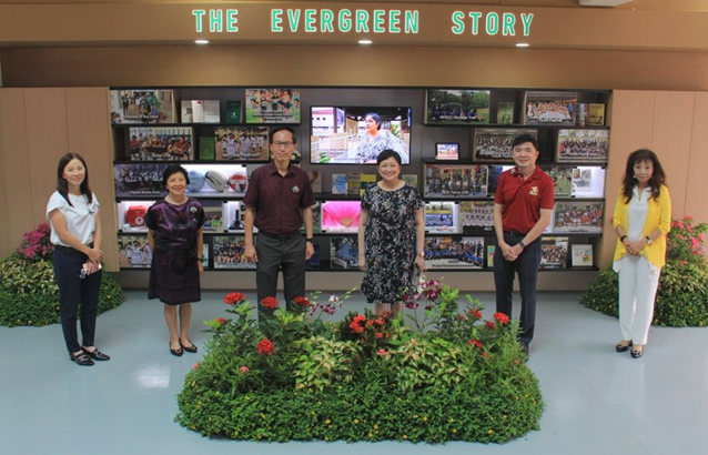 Six people stand around a flower display in front of a wall reading "The Evergreen Story" with photos.